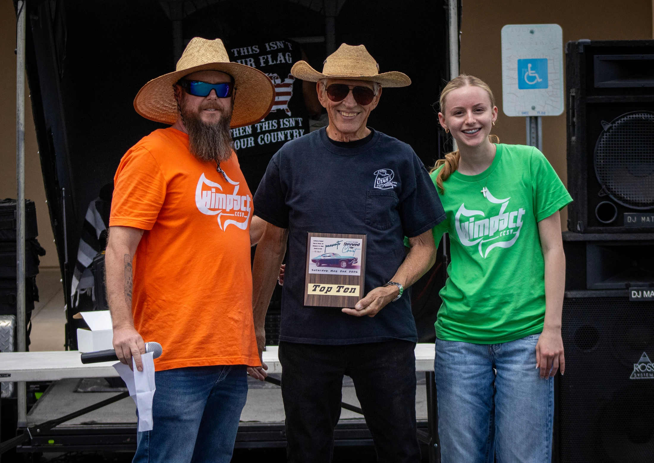 Two men and a young woman stand together for a photo. The man in the center holds a 'Top Ten' award plaque and smiles, flanked by the others.