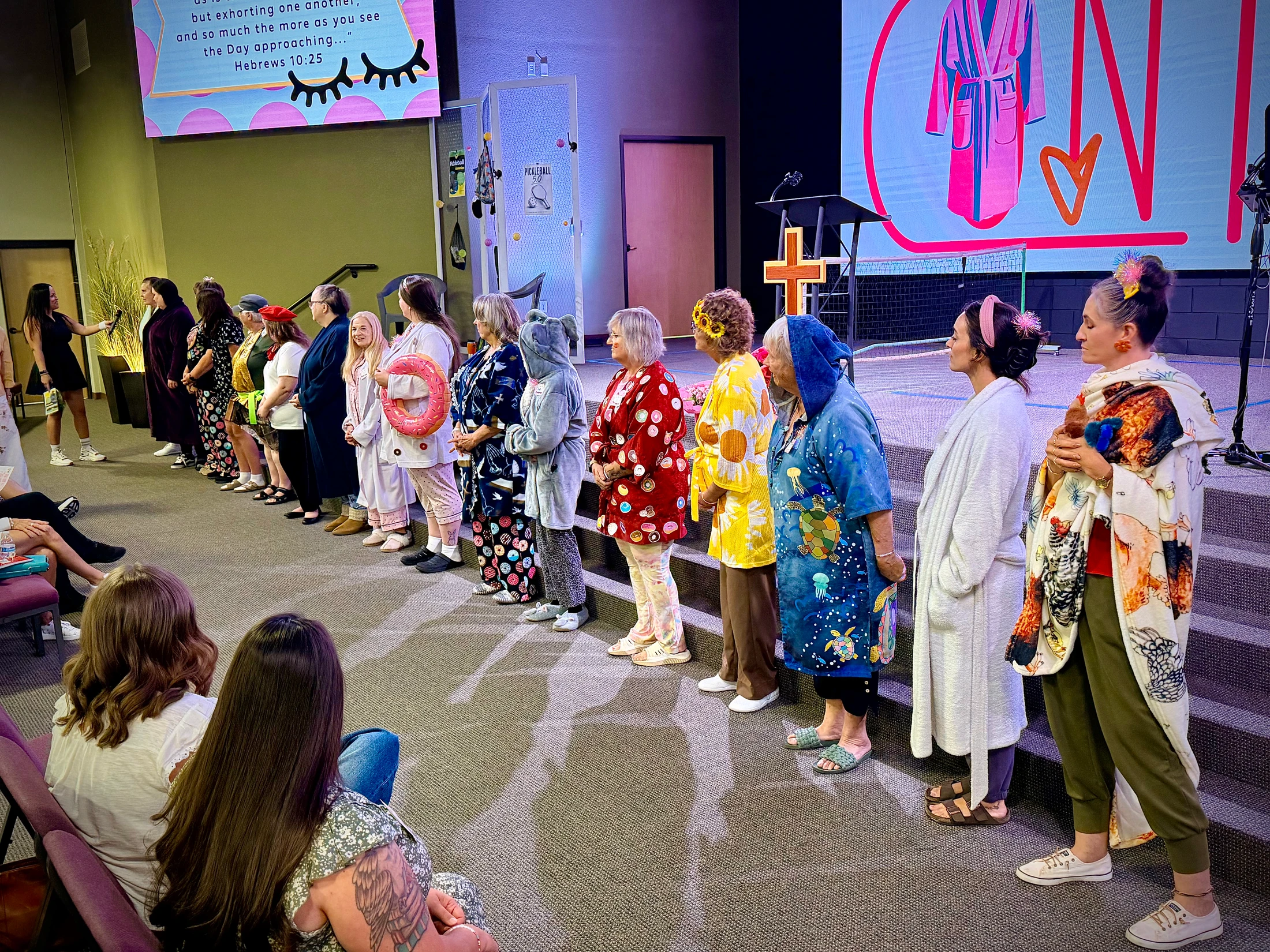 A line of women on a church stage show off their creative and colorful pajamas and robes to an audience during a women's ministry event.