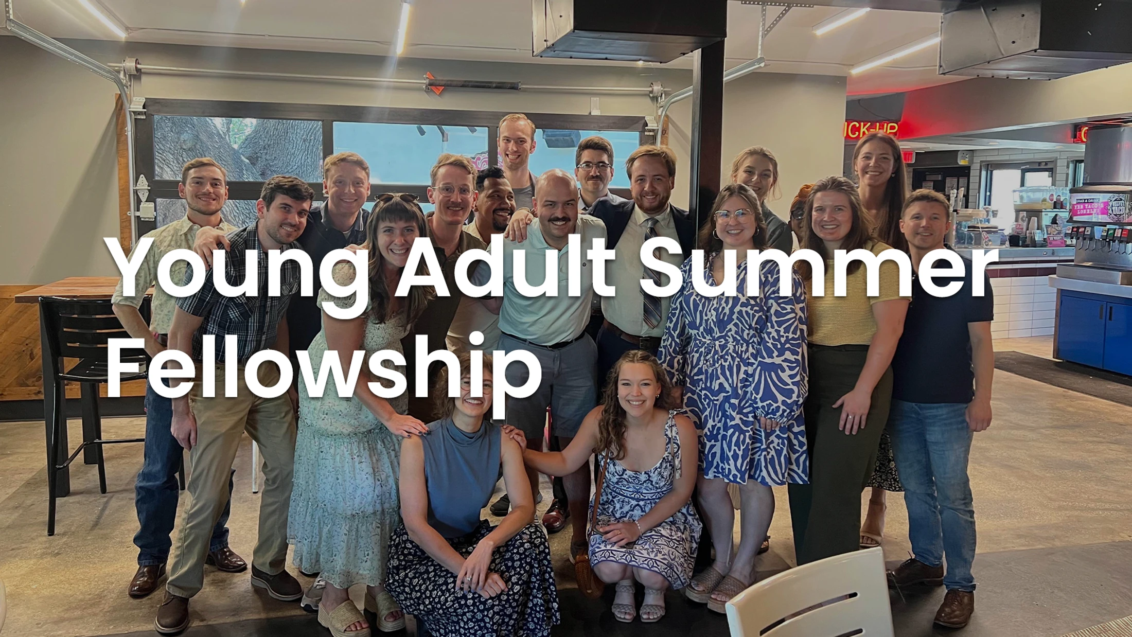 A large group of smiling young adults pose together for a photo indoors at a restaurant. White text over the image reads 'Young Adult Summer Fellowship'.