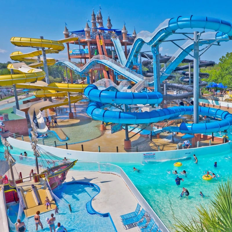 A vibrant water park on a sunny day, featuring towering blue and yellow slides, a castle structure, and people swimming in the pools below.