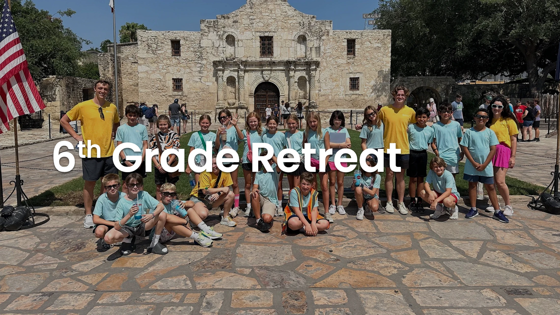 A large group of sixth-grade students and their chaperones smile for a group photo in front of the historic Alamo building in Texas during a school retreat.
