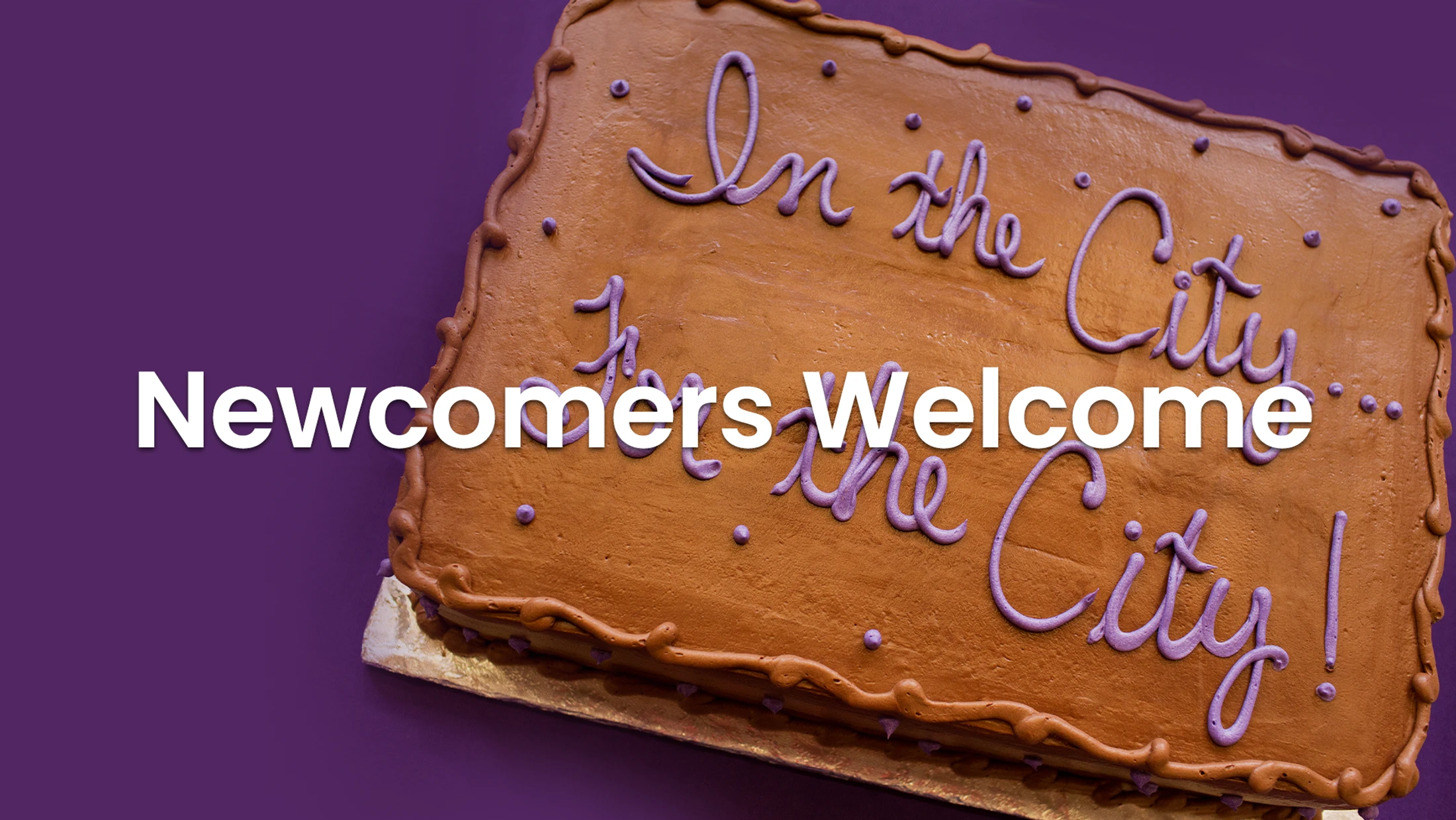 A chocolate cake on a purple background with the text 'Newcomers Welcome' overlaid. The cake is decorated with purple icing that says 'In the City'.