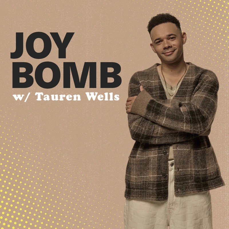Tauren Wells, host of the Joy Bomb podcast, smiles with his arms crossed. He wears a brown plaid cardigan against a tan background with yellow dot patterns.