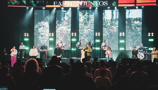A worship band performs on a brightly lit stage in front of a large screen reading 'EASTER JUNTOS'. The audience watches from the foreground.