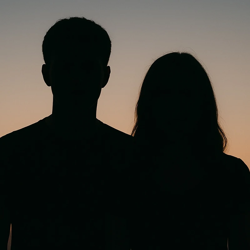 The silhouettes of a man and a woman standing side by side against a gradient sky of soft orange and blue at dusk. Their features are completely in shadow.