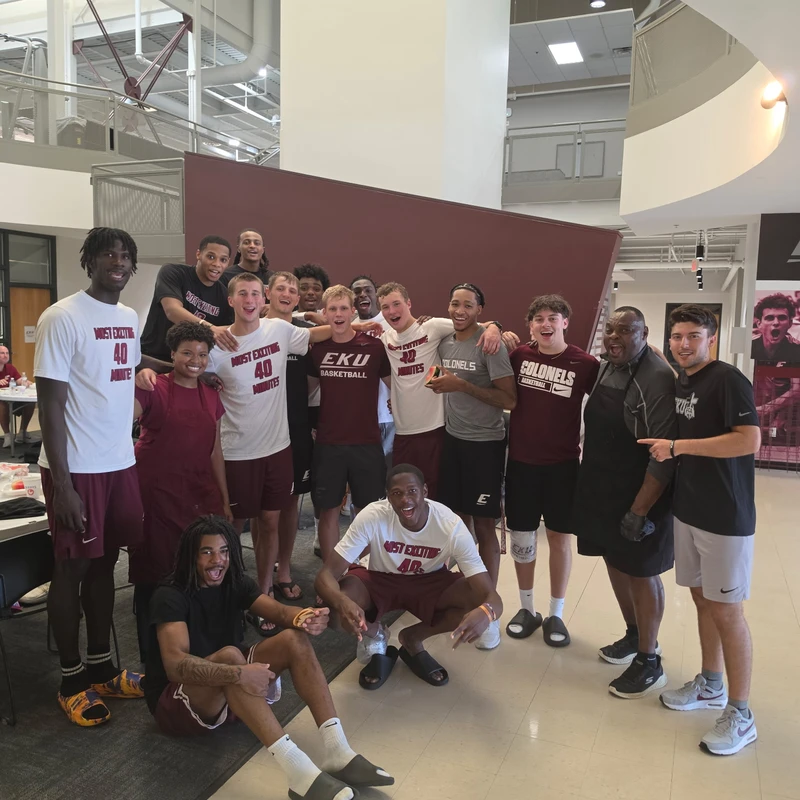The Eastern Kentucky University men's basketball team and staff pose for a happy group photo indoors, wearing EKU Colonels apparel.