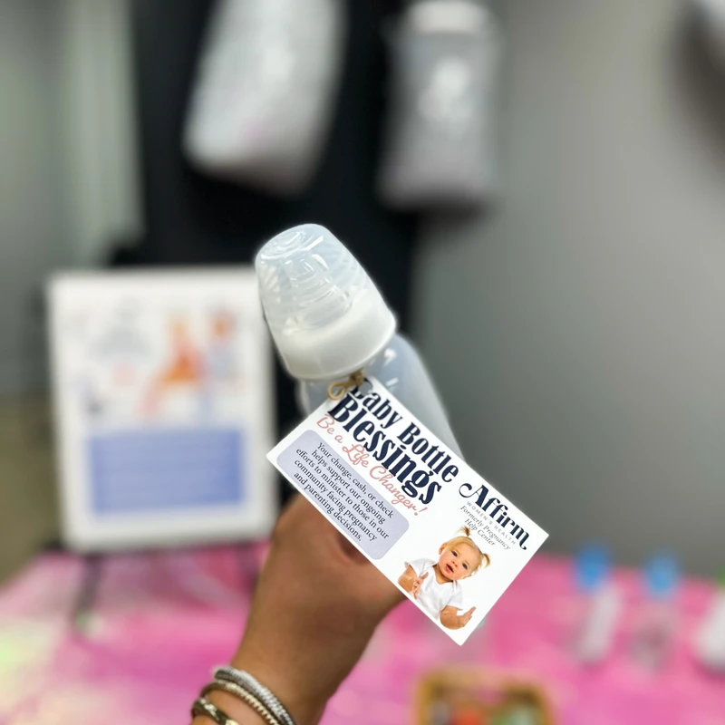 A person holds up a baby bottle with a tag for the 'Baby Bottle Blessings' fundraiser, which supports a local pregnancy and parenting center.