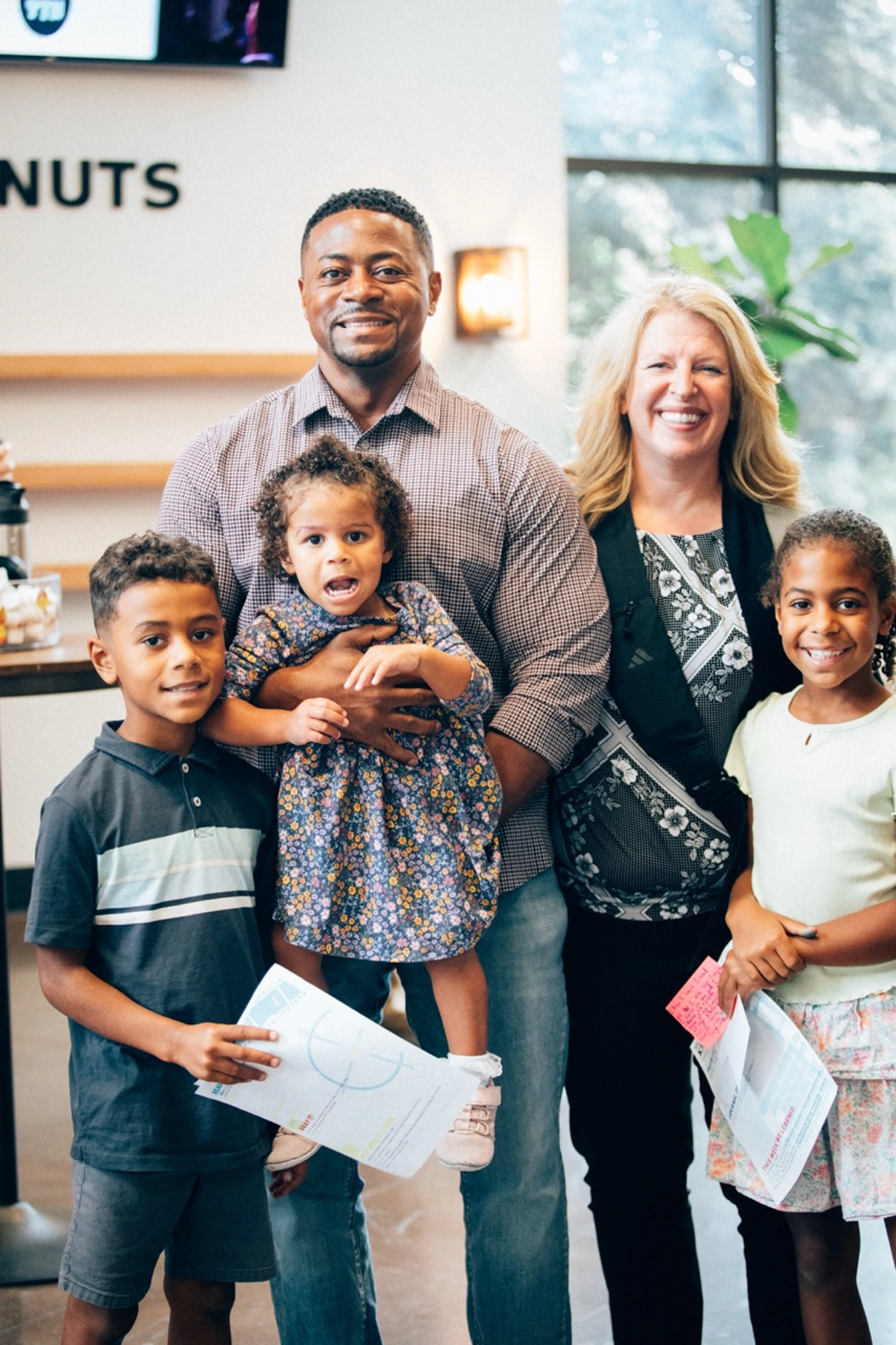 A happy, mixed-race family of five smiles for the camera. A man holds a toddler girl, next to a woman, with a young boy and girl standing in front.