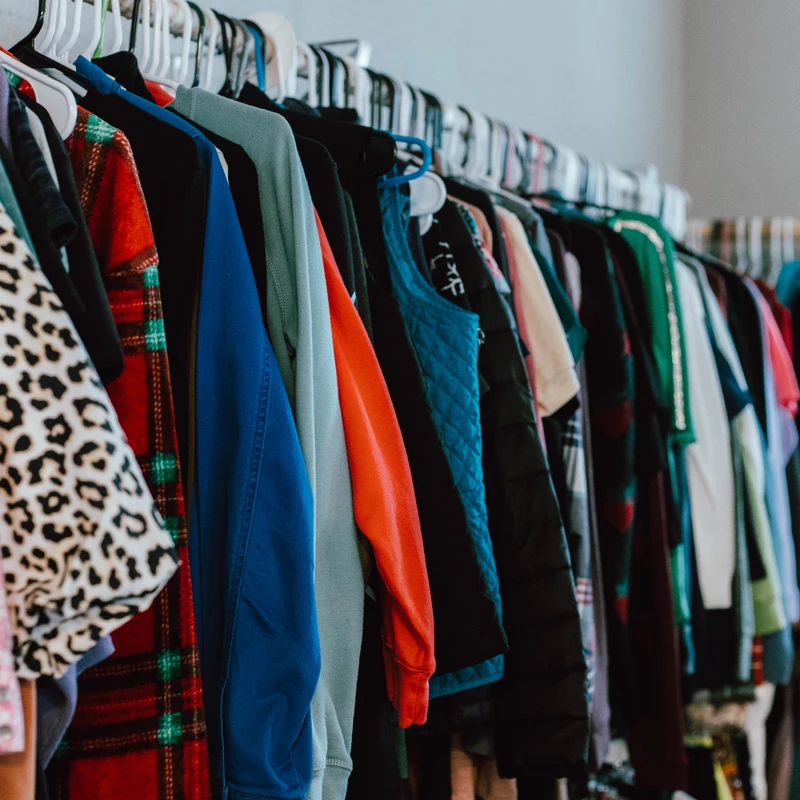 A clothing rack filled with a variety of colorful and patterned clothes, including leopard print and plaid, hanging on white hangers.