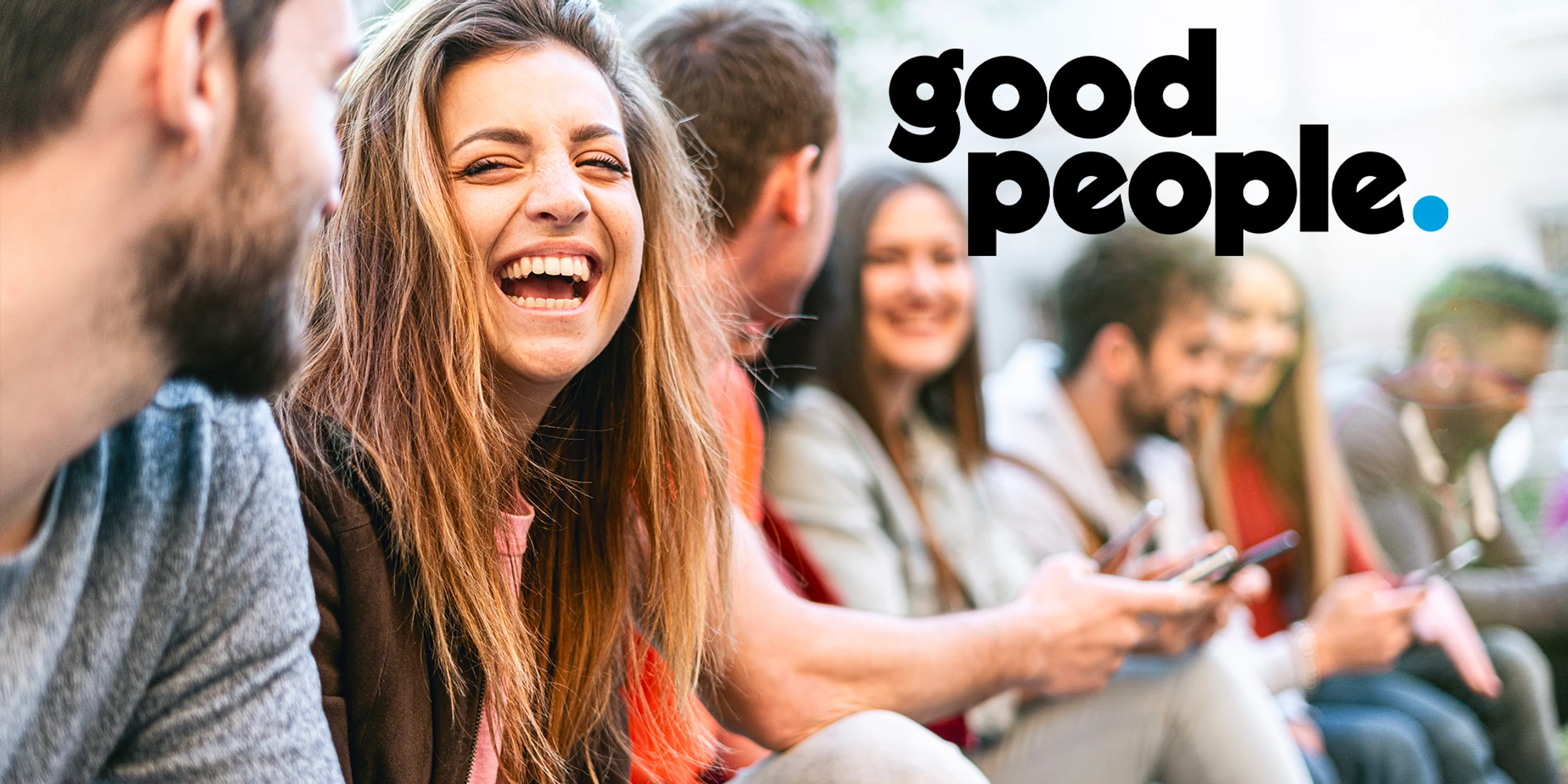A young woman with long hair laughs while sitting with a group of friends. The text 'good people.' is overlaid on the right side of the image.