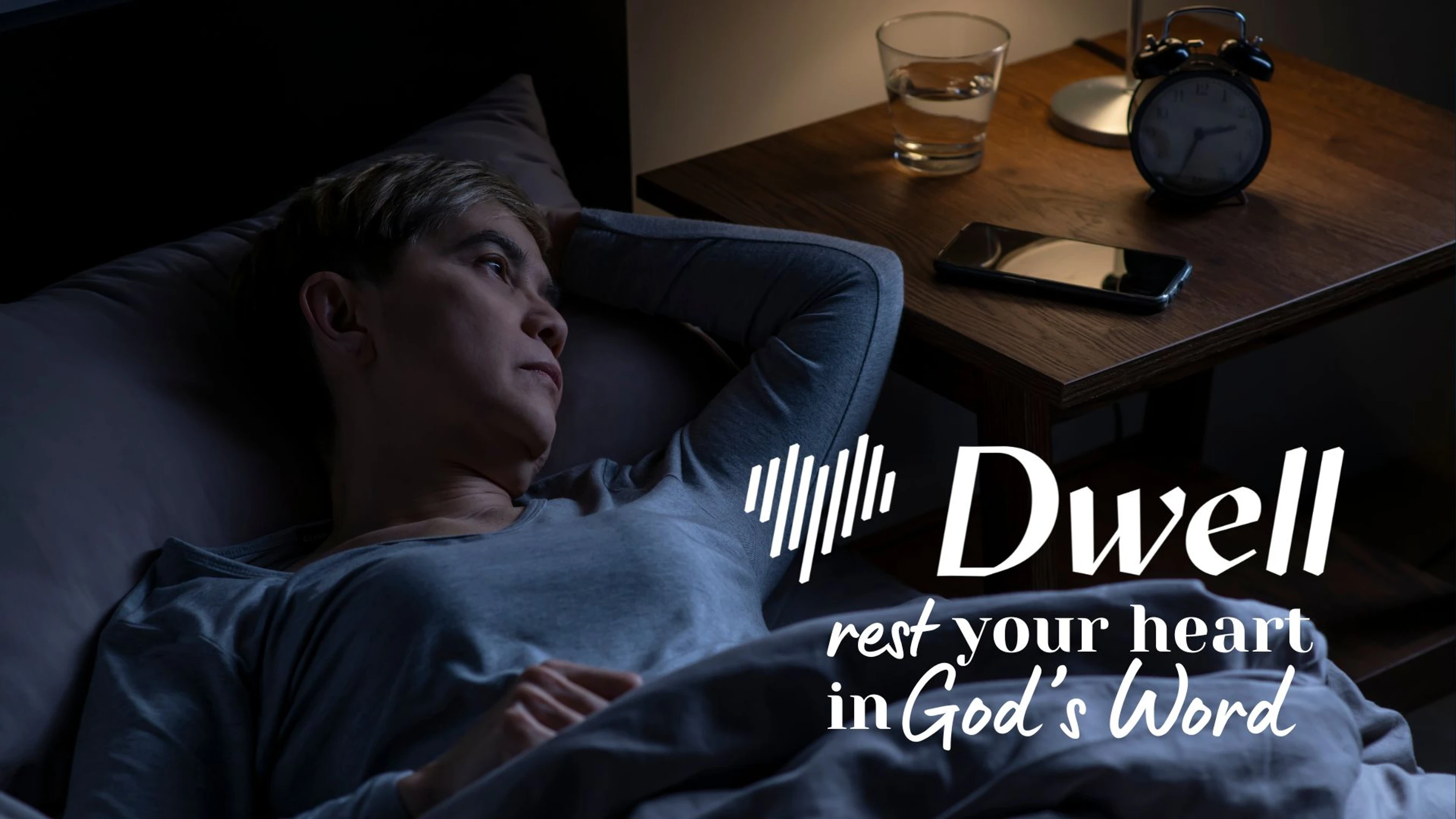 A person lies awake in bed at night, looking worried. The image has a logo for the Dwell app and text that reads, "rest your heart in God's Word."