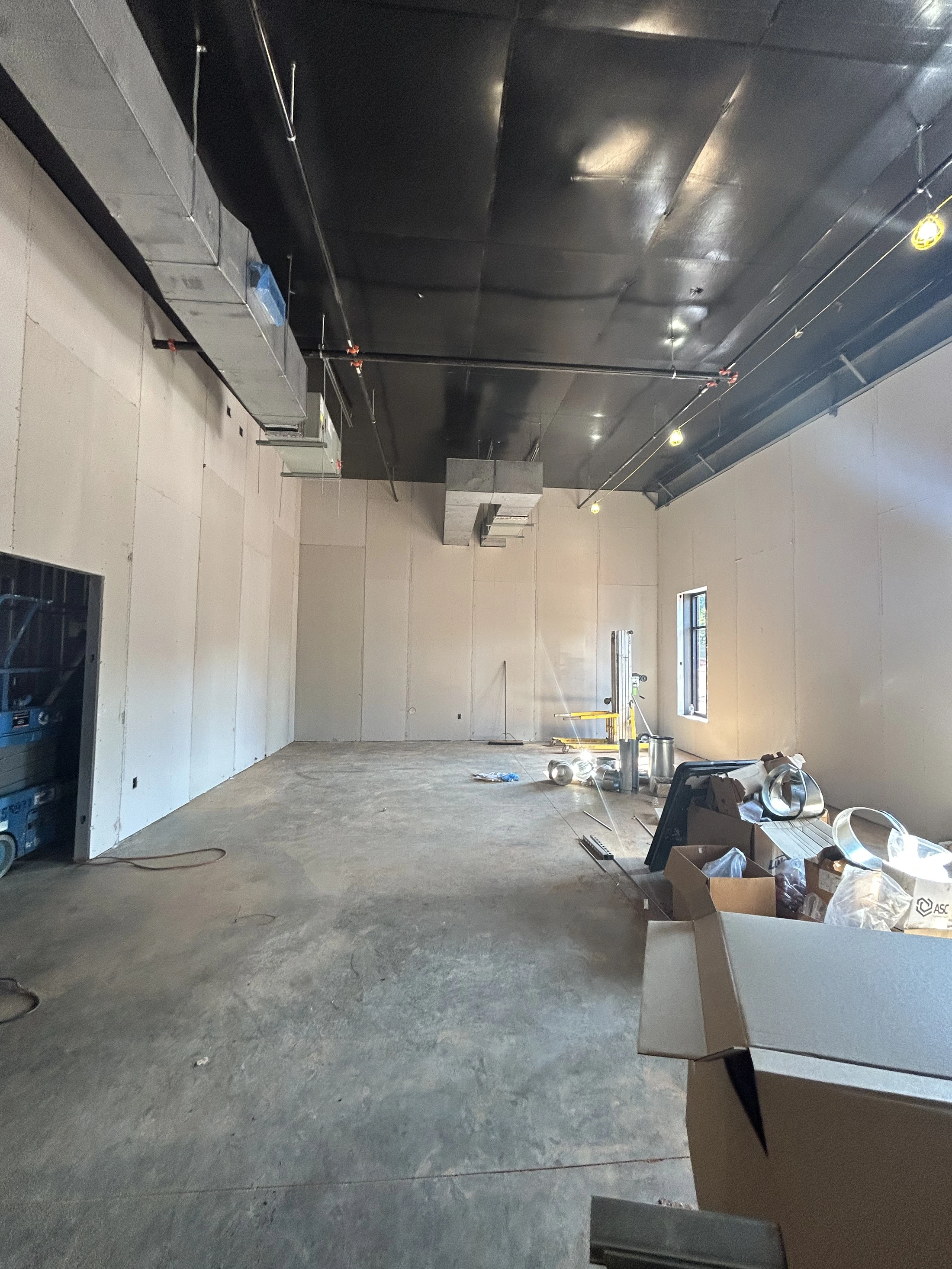 An empty commercial space under construction with concrete floors, unfinished drywall, and an exposed black ceiling with silver HVAC ductwork.