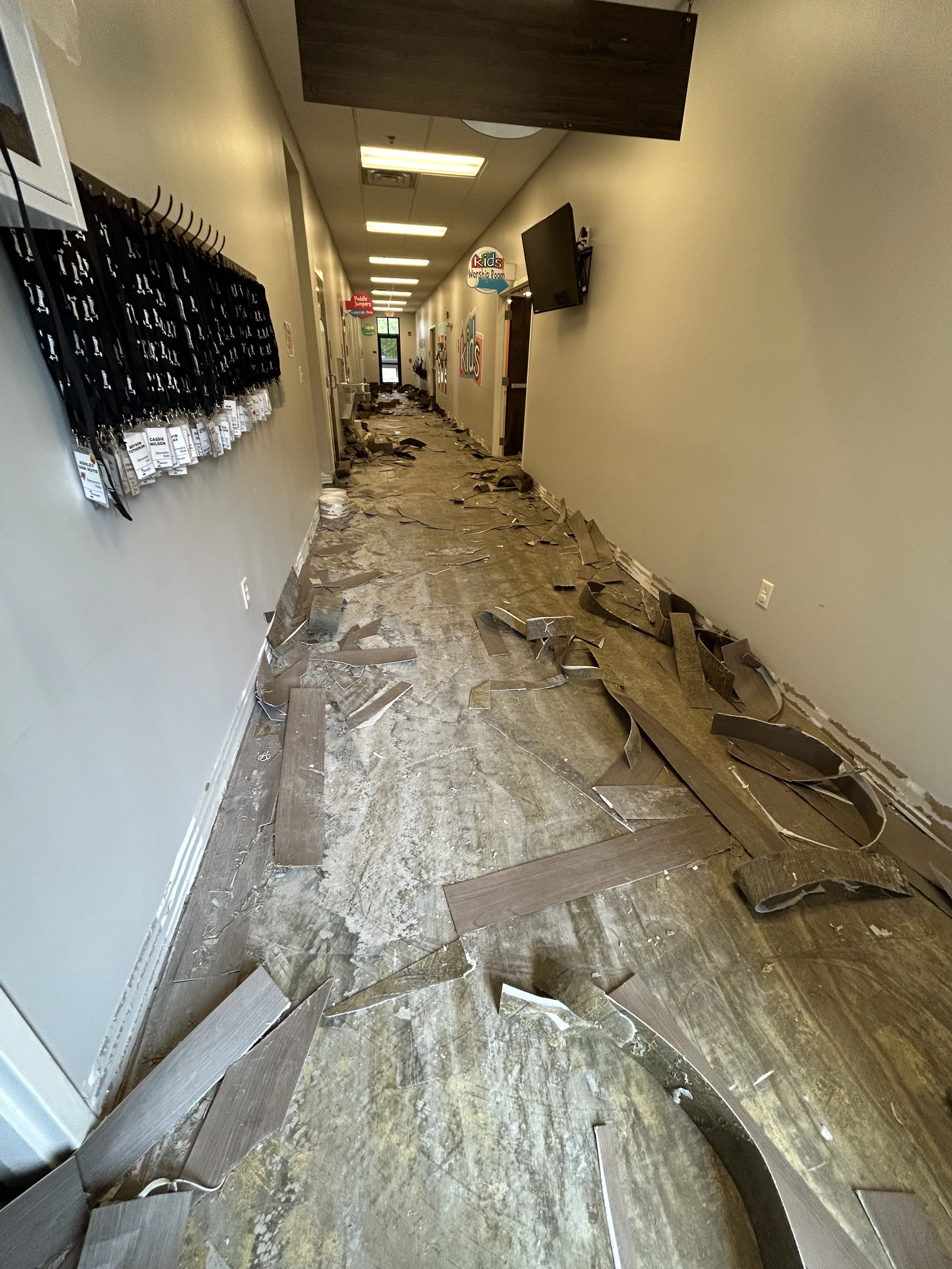 A long hallway in a building where the laminate flooring has been completely ruined, peeling up in broken pieces and scattered across the subfloor.