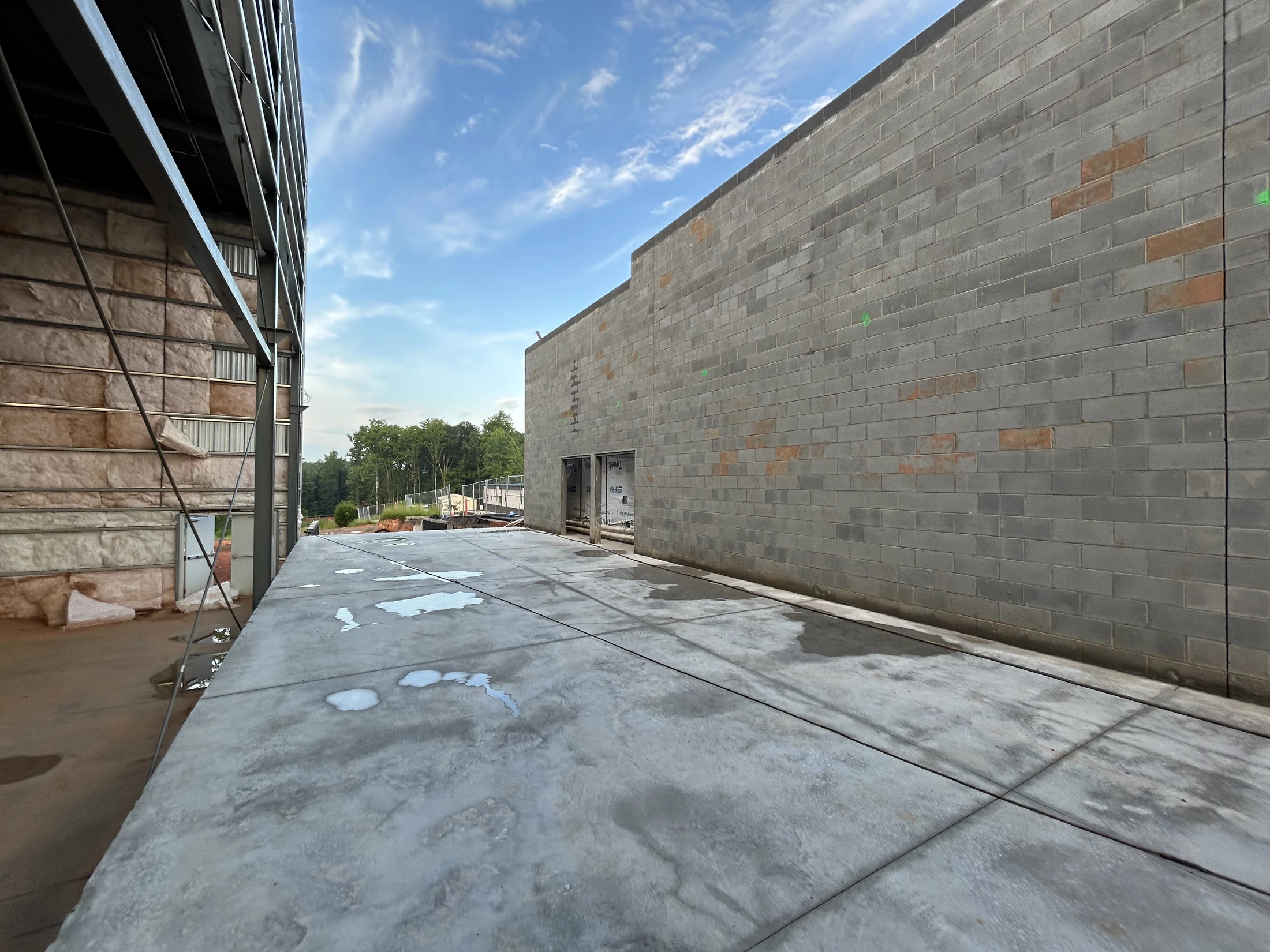 A wide-angle view of a building construction site. A concrete block wall is on the right, and a steel-framed wall with insulation is on the left.